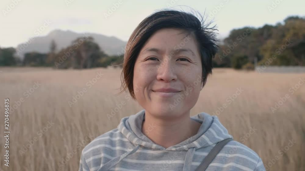 Asian woman standing in field shy smile into camera