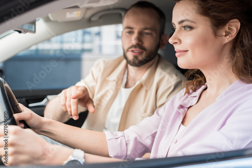 selective focus of handsome man pointing with finger at steering wheel near happy woman in car