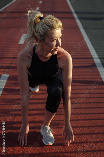 Beautiful happy blonde woman in black sportswear doing exercising on the bridge above the river at sunset.