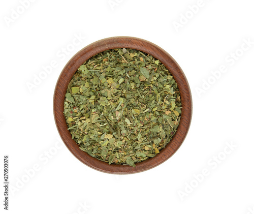 Dried parsley in a wooden bowl on a white background. Top view