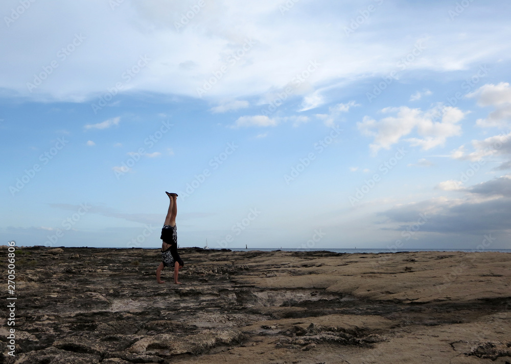 Man Handstands on shore rocks of Ko Olina