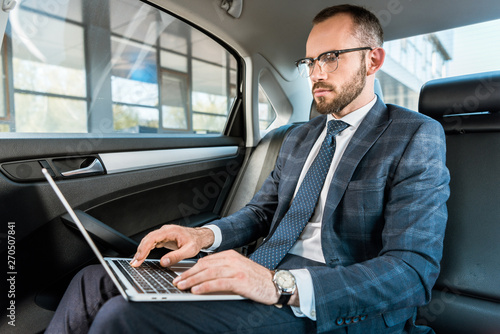 low angle view of handsome businessman in glasses typing on laptop in car © LIGHTFIELD STUDIOS