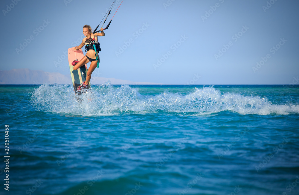 Kite surfing girl in sexy swimsuit with kite in sky on board in blue