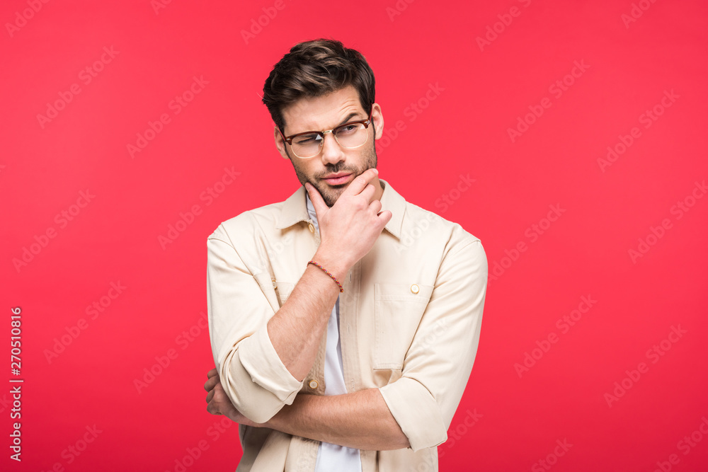 pensive man in glasses touching chin isolated on pink