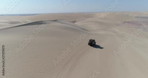 4K aerial rear view of a 4x4 vehicle driving along the sand dunes of the Skeleton Coast, Namib desert, Namibia photo