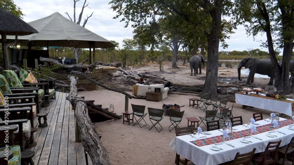 4K panning view of deck and outside dinner table with elephants drinking at the waterhole in front of Khwai Private Reserve, Botswana 4K panning view of deck and outside dinner table with elephants drinking at the waterhole in front of Khwai Private Reserve, Botswana