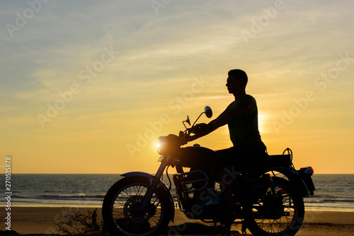 Silhouette of guy on motorcycle on sunset background. Young biker are sitting on motorcycle, face in profile. Moto trip on the seaside, freedom and active lifestyle.