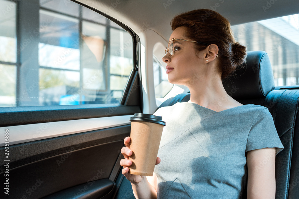 low angle view of woman in glasses holding paper cup while sitting on car