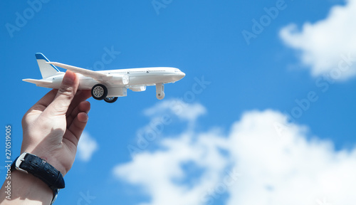 Hand holding airplane model in front of blue sky background. Travel