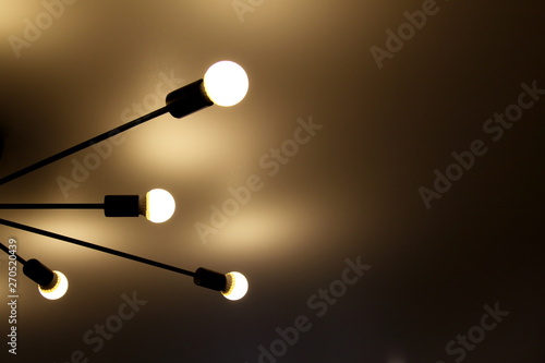 a chandelier of bright light bulbs on black beams on the ceiling and light background