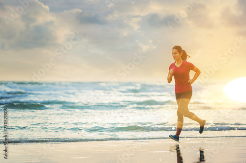 Woman running at the beach with sunset background. © Panumas