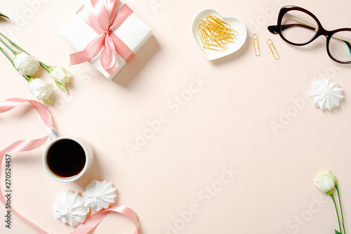 Flat lay home office desk. Female workspace with ribbon, coffee cup, gift box, marshmallows and roses on pink background. Top view feminine background with copy space for text.