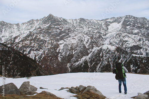 A young man trekking across the Himalayan region of Triund,Himachal pradesh, India with a heavy bag pack on his back. photo