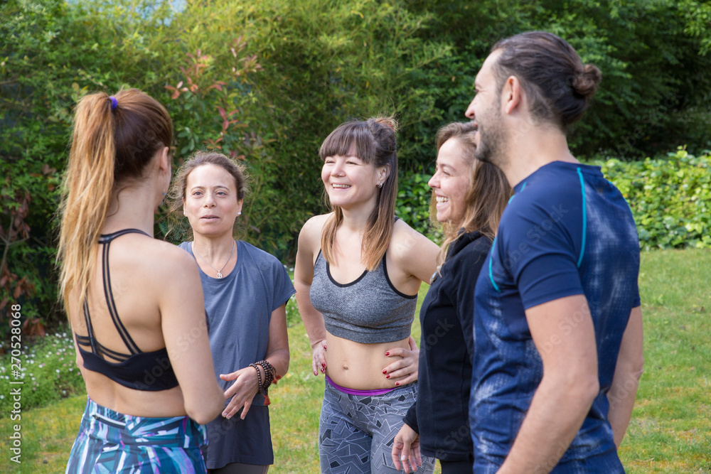 Team of positive yogis chatting in park. Man and women in fitness apparels standing outdoors and talking. Yoga and communication concept Team of positive yogis chatting in park. Man and women in fitness apparels standing outdoors and talking. Yoga and communication concept