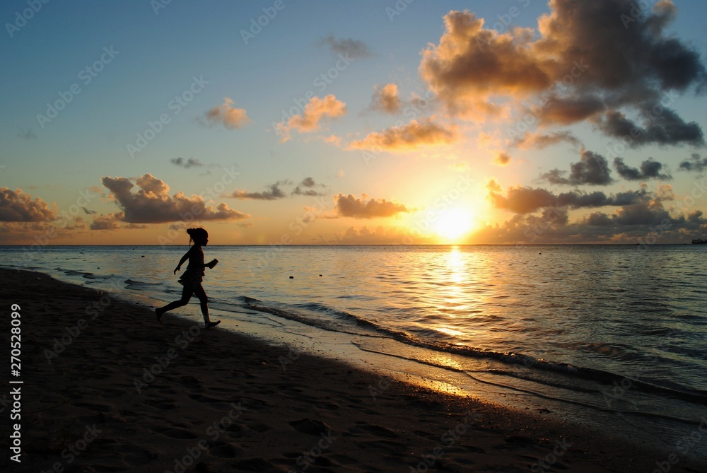 Silhouette of an unrecognizable girl running on the beach at sunset, with golden reflections in the water