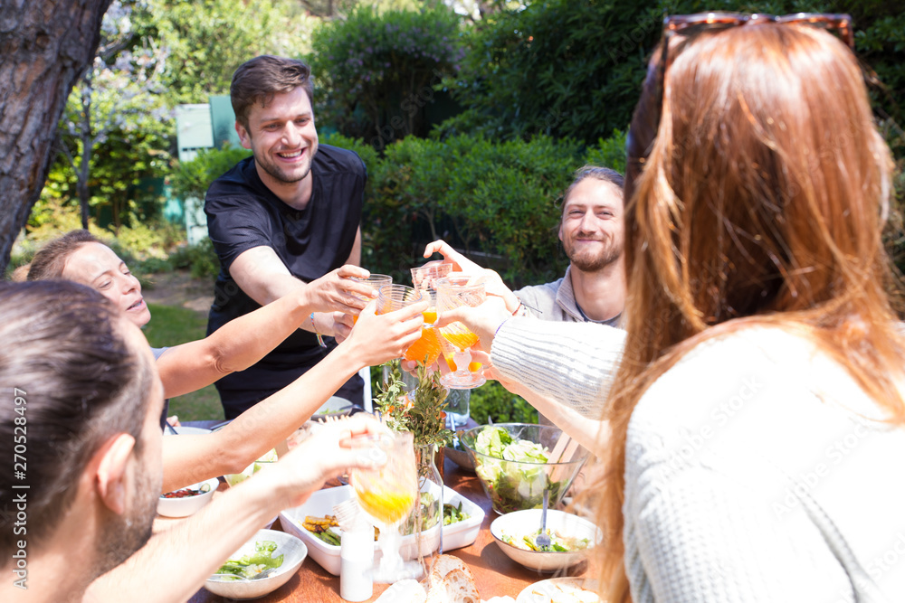Portrait of happy young friends toasting juice at garden party. Young people having dinner outdoors in springtime. Outdoor party concept Portrait of happy young friends toasting juice at garden party. Young people having dinner outdoors in springtime. Outdoor party concept
