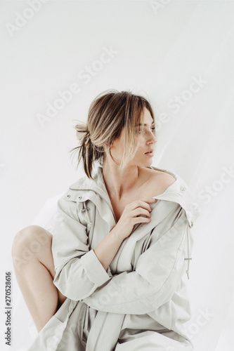 Beautiful woman in white cloak sitting and looking to the sideon a white background photo