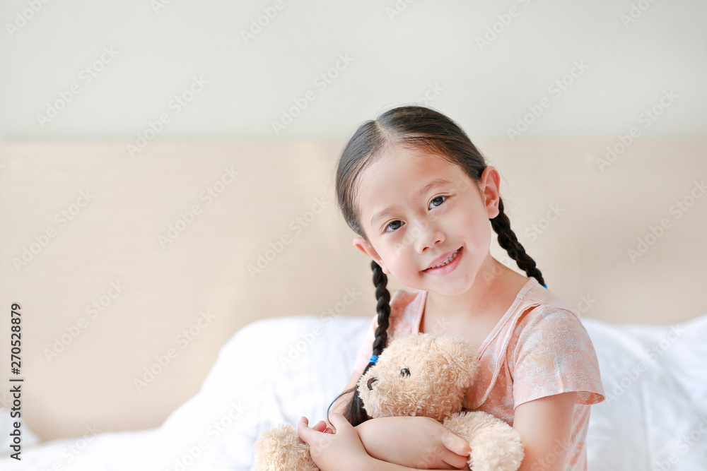 Smiling Asian little girl cuddle teddy bear sitting on the bed at home. Smiling Asian little girl cuddle teddy bear sitting on the bed at home.