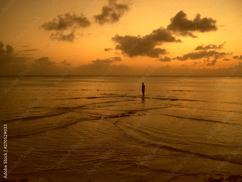 Golden ripples and waves in the beach at sunset, with an unrecognizable person standing in the distance. 