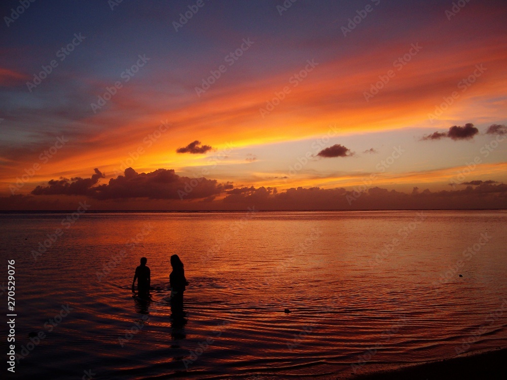 Breathtaking sunset in the beach with two unrecognizable people standing in the water 