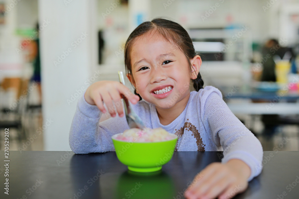 Smiling little Asian girl enjoy eating ice cream in cup sitting on the table in cafe. Smiling little Asian girl enjoy eating ice cream in cup sitting on the table in cafe.