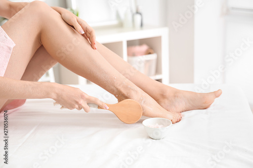 Young woman applying body scrub at home