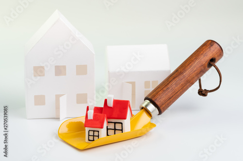 Housing price growing, real estate, architecture construction building or mortgage loan concept, small cute miniature house with red roof on yellow post hole digger shovel on white background photo