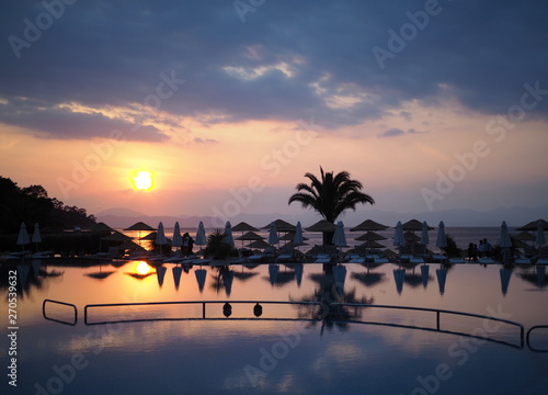Fototapeta Naklejka Na Ścianę i Meble -  Dalaman - Turkey - May 2019 – Palm Tree On A Beach With Sunset Behind At the Hillside Beach Club in Fethiye.    