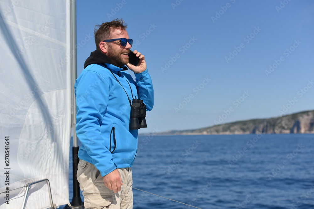 Obraz premium Man sailing with sails out on a sunny day and talking on the phone