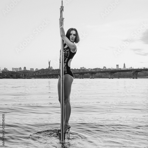 portrait of athletic beautiful redhead woman with long hair on the pole in river Dnieper on cityscape background in the evening (sunset)