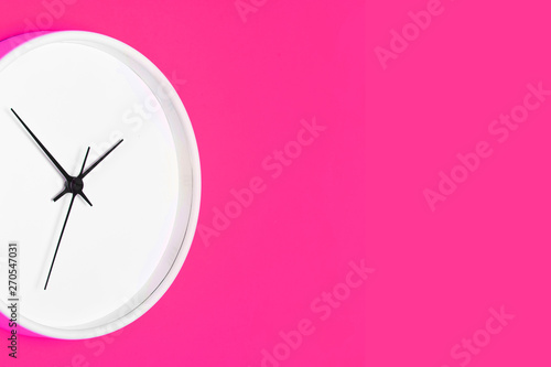 White round clock with black numbers isolated on pink paint wall. Empty copy space time background.