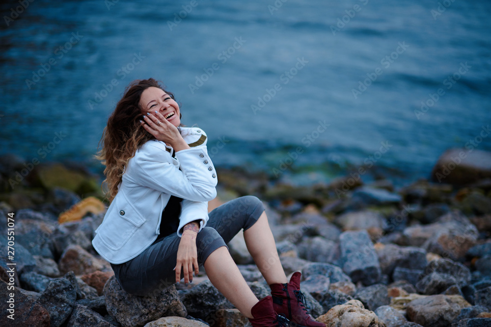 fashionable girl dressed in white jacket and wide trousers posing near sea in the evening
