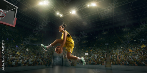 Female basketball player makes slam dunk. Basketball player on big professional arena during the game © Alex