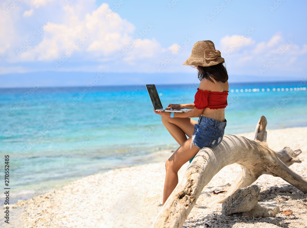Asian young woman with red coth and hat which she is a  using laptop computer on a beach. Freelance work concept