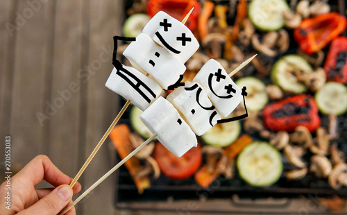 Funny marshmallow on sticks over grilled vegetables on bonfire