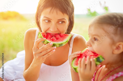 Two smiling girls eats slice of watermelon outdoors on meadow. Mother and daughter spend time together. Diet  vitamins  healthy food concept.