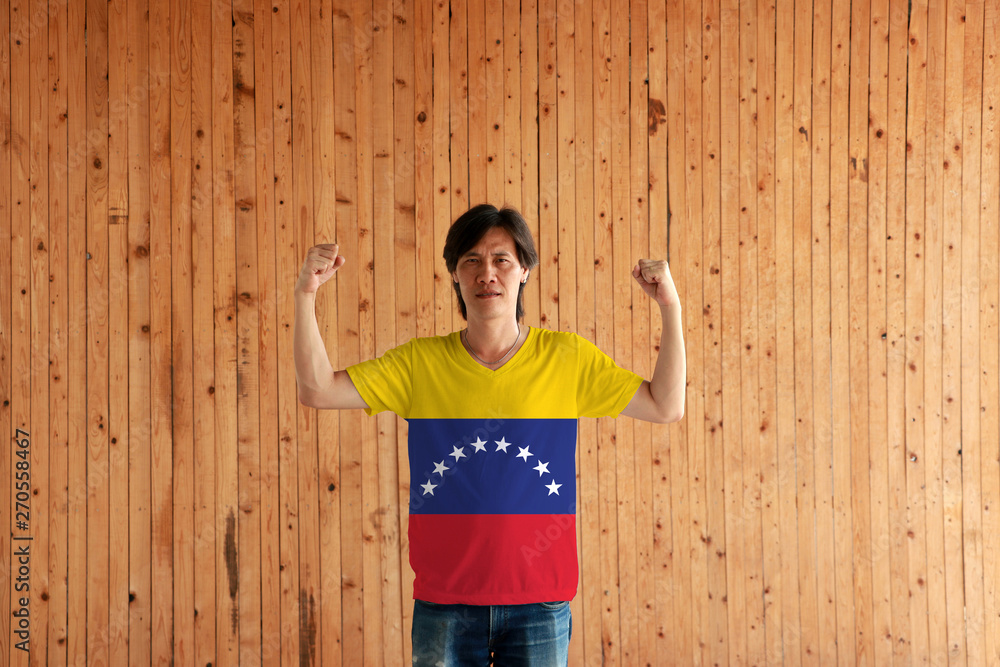 Man wearing Venezuela flag color of shirt and standing with raised both fist on the wooden wall background. Man wearing Venezuela flag color of shirt and standing with raised both fist on the wooden wall background.