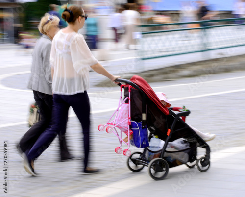 Fototapeta Naklejka Na Ścianę i Meble -  Young mother with small child in the stroller walking down the s