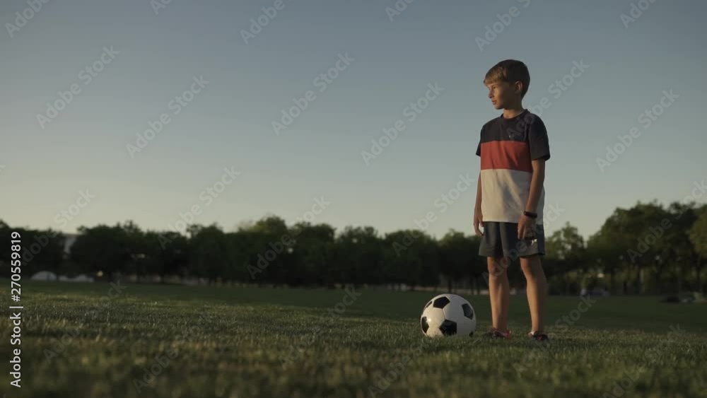 portrait of a boy football player with a ball in a park standing on the lawn looking at the camera portrait of a boy football player with a ball in a park standing on the lawn looking at the camera