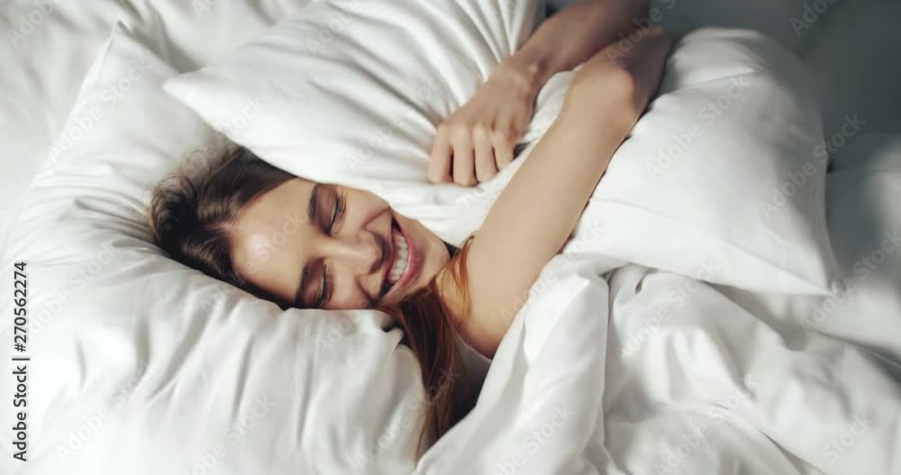 Happy smiling caucasian woman stretching in bed while waking up in sunny bedroom, close up indoors Happy smiling caucasian woman stretching in bed while waking up in sunny bedroom, close up indoors