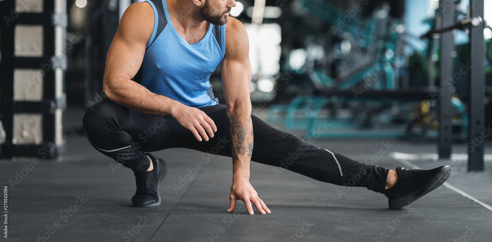 Fototapeta premium Man stretching leg before workout at gym