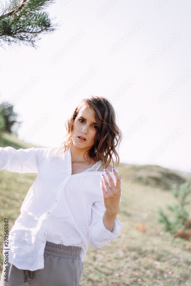 Beautiful young woman in white near a tree in rural sunny landscape background in summer. Tender happy woman in enjoying nature. Soft focus Beautiful young woman in white near a tree in rural sunny landscape background in summer. Tender happy woman in enjoying nature. Soft focus