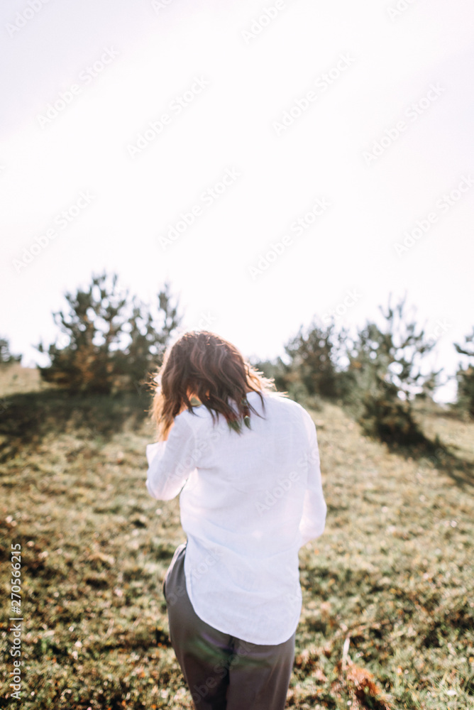 Beautiful young woman in white collecting grass at the rural sunny landscape background in summer. Tender happy woman in wild field enjoying nature. Back view Beautiful young woman in white collecting grass at the rural sunny landscape background in summer. Tender happy woman in wild field enjoying nature. Back view