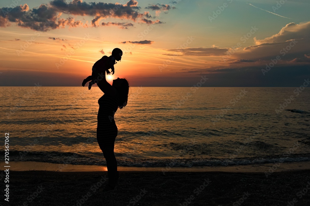young mother raises a child in her arms at sunset