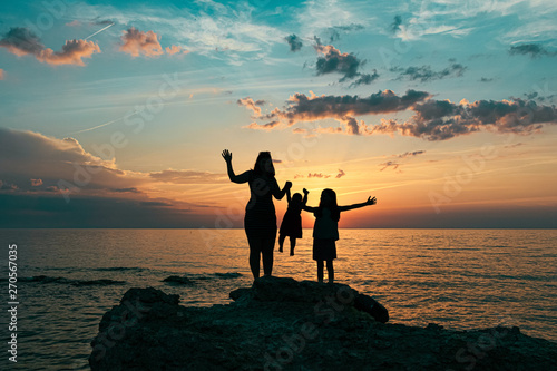 silhouettes of mom with daughters. mother with two daughters hold hands at sunset.