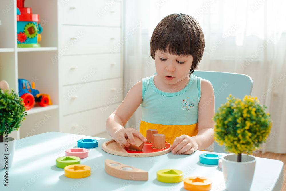 little girl collects a wooden unpainted pyramid. Safe natural wooden children's toys. little girl collects a wooden unpainted pyramid. Safe natural wooden children's toys.