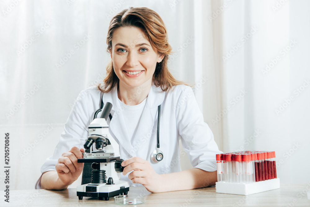 doctor in white coat with stethoscope using microscope in clinic