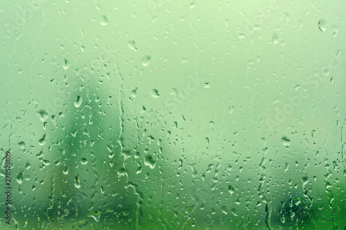 Rain drops on window with green tree as background. Natural water drops on glass. Selective focus