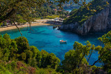Beautiful landscape with sea and small boat on a water surface, beach, mountains and cliffs, green trees and bushes, rocks in a blue water. Corfu Island, Greece. 