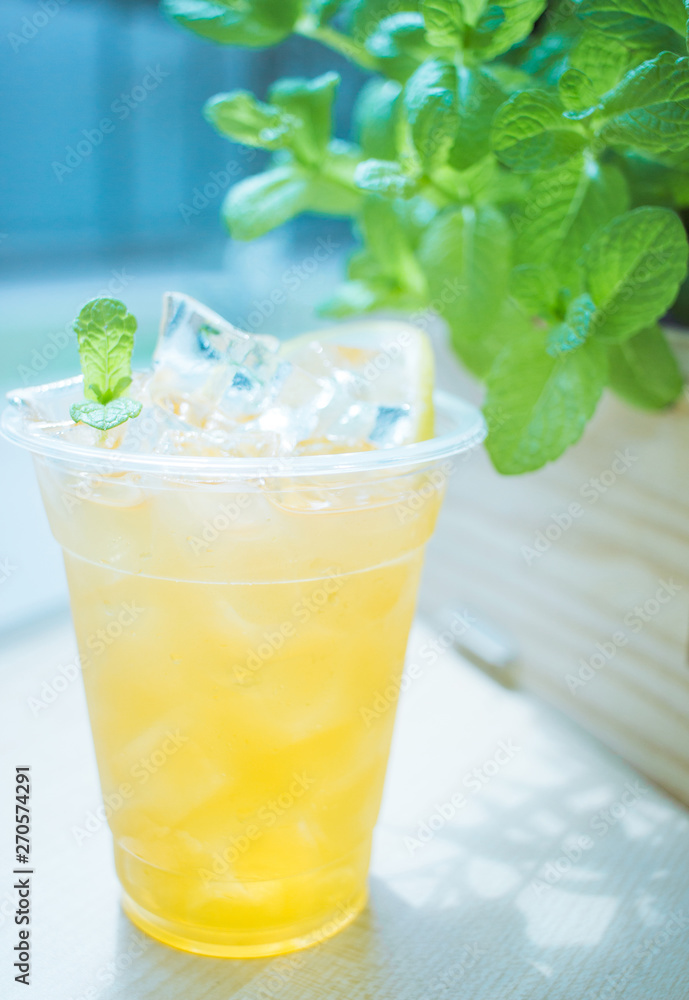 Black tea lemonade, lots of ice and a slice of lemon.In the background are green mint leaves in the sun.The drink is sweet and sour Black tea lemonade, lots of ice and a slice of lemon.In the background are green mint leaves in the sun.The drink is sweet and sour